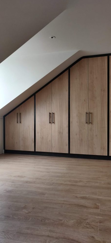 Natural Kendal Oak fitted wardrobes Modern room with sloped ceiling, featuring wooden cabinetry along one wall.