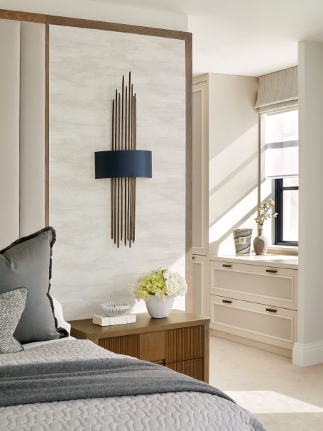 Cremé Beige tall storage with lower drawers Stylish bedroom featuring a light-coloured wall, modern lamp, and wooden furniture.