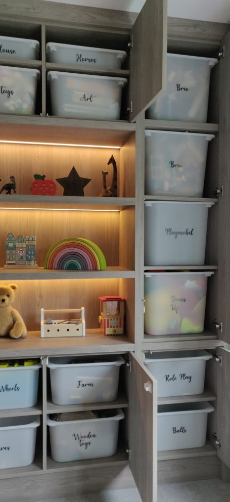 Grey Nordic Wood open shelving with LED's. Surrounding storage A modern room with a wooden shelf displaying various toys and decorative items.