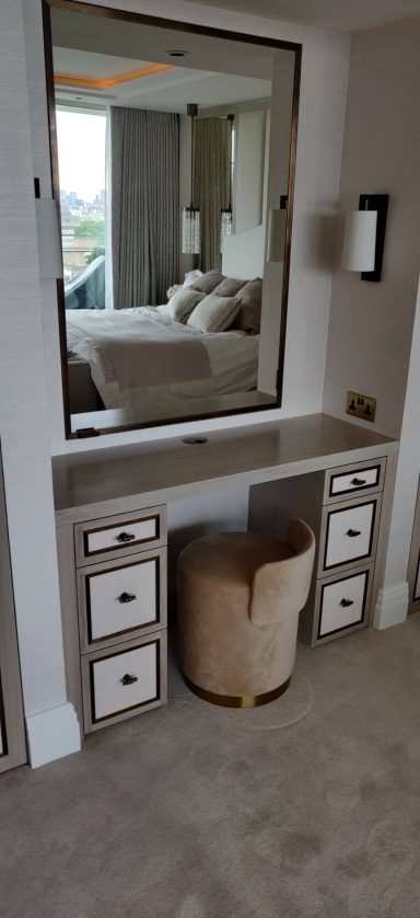 Stained oak dressing table with antique brass trimming Dressing table with a large mirror, drawers, and a round upholstered chair.