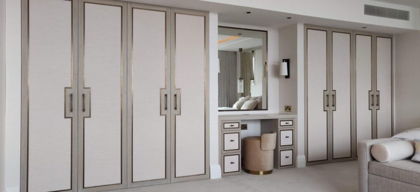 Stained oak wardrobe and dressing table with antique brass trimming Luxury bedroom featuring elegant wardrobes, a mirror, and a stylish dressing area.