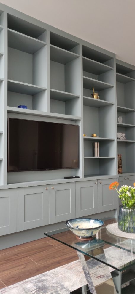 Fijord Green display shelving with central TV panel Modern living room with a grey bookshelf, TV, and a glass dining table with flowers.