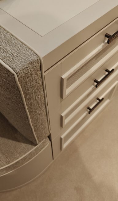 Cremé Beige walk-in dressing room with upholstered island A close-up of a beige desk with drawers and a textured fabric covering.