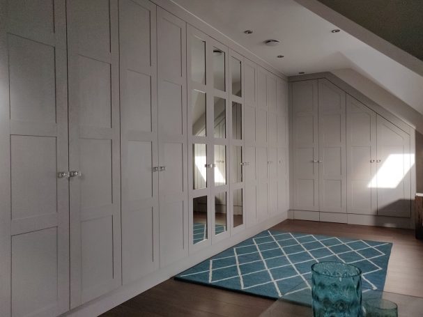 Cashmere Grey wardrobe with frame and panel doors. Bright attic space with white wardrobes, a large mirror, and a blue patterned rug.