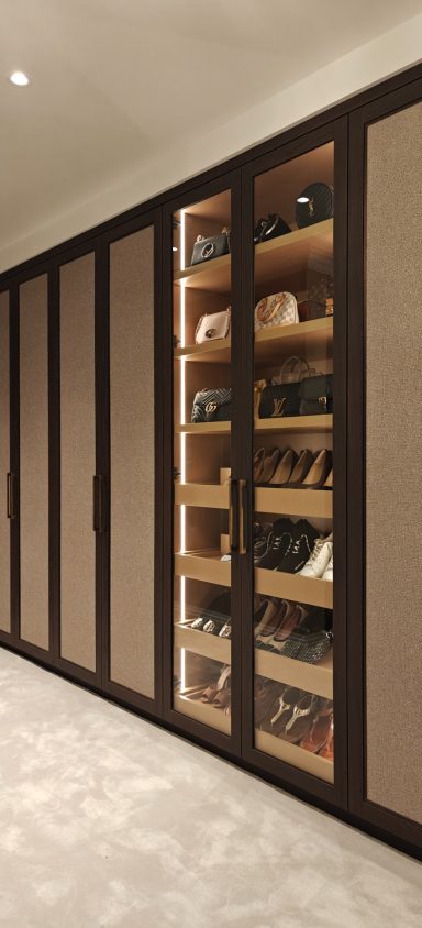 Brown Albano Ash dressing room with shoe display cabinets. A modern wardrobe featuring shelves of shoes and handbags against a neutral wall.