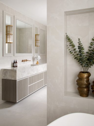 Grey Vicenza vanity with storage cabinet and two central drawers. Flush mirrored wall cabinets. Modern bathroom featuring a grey vanity, gold accents, and a decorative plant in a vase.