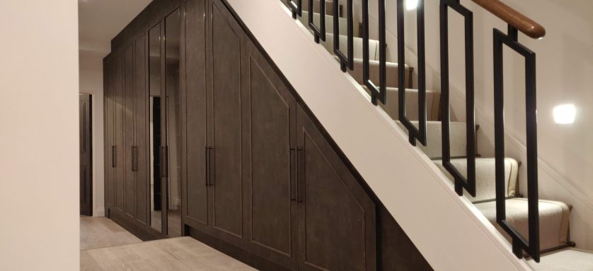 Ares understair storage with antique brass door trimming. A modern hallway featuring a staircase with wooden steps and black railings.