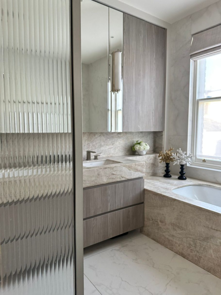 Grey Nordic four drawer vanity with mirrored wall cabinet. Modern bathroom with a sink, mirror, and a bathtub, featuring neutral tones and natural light.