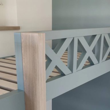 Fjord Green and Oak bunk beds, top rail detail. Light blue wooden railing with a diagonal cross pattern, adjacent to a beige wall.