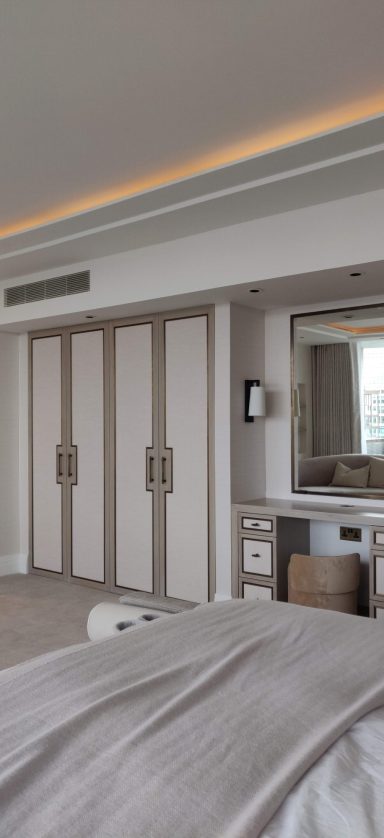 Stained oak wardrobe and dressing table with antique brass trimming Modern bedroom with a large mirror, wardrobe, and neutral decor.