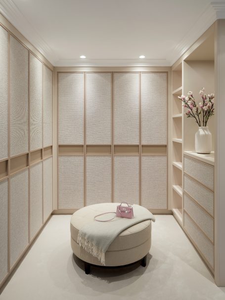 Sand Beige dressing room. Wallpapered doors with integrated handles Minimalist room with light wooden cabinetry, a round ottoman, and floral décor.
