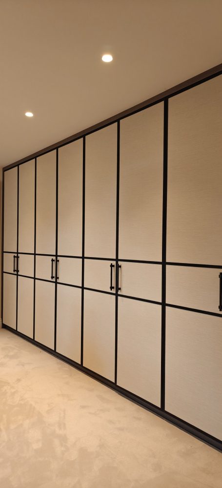 Grey Vicenza Oak dressing room doors with wallpapered panels Modern wardrobe with beige doors and sleek black frames in a minimalist interior.