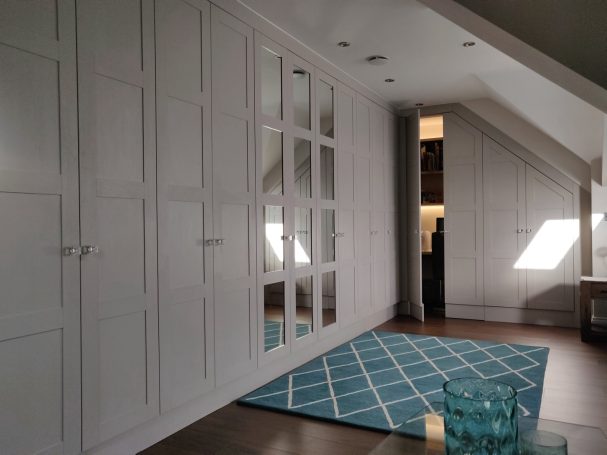 Cashmere Grey wardrobe with hidden home office. Bright attic space with white cabinets and a teal patterned rug.