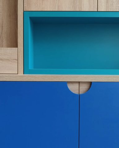 Handle detail for lower storage cabinets. Wooden furniture with a blue and teal drawer design.