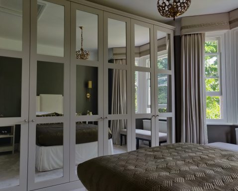 Shaded White wardrobe with frame and mirrored panel doors Modern bedroom with a large mirrored wardrobe and elegantly arranged bed.
