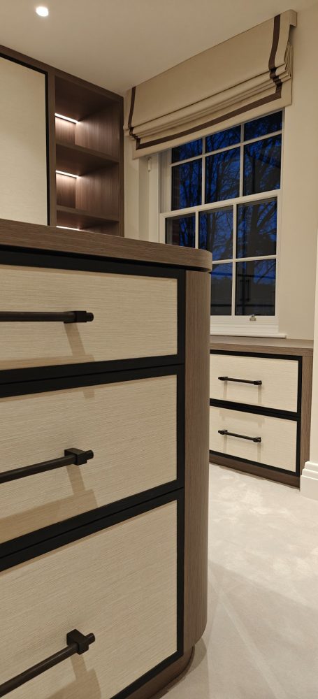 Grey Vicenza Oak dressing room island with drawers Modern bedroom featuring stylish cream and brown furniture, with a window and blinds.