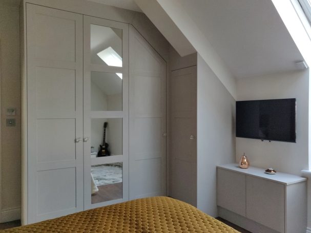 Cashmere Grey corner wardrobe with frame and panel doors Modern bedroom with a large wardrobe, TV on the wall, and a warm bedspread.