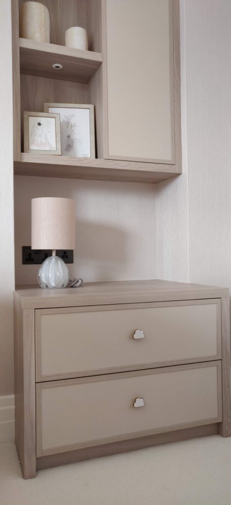 Tivoli two drawer side table A light beige bedside table with two drawers and a lamp on top.