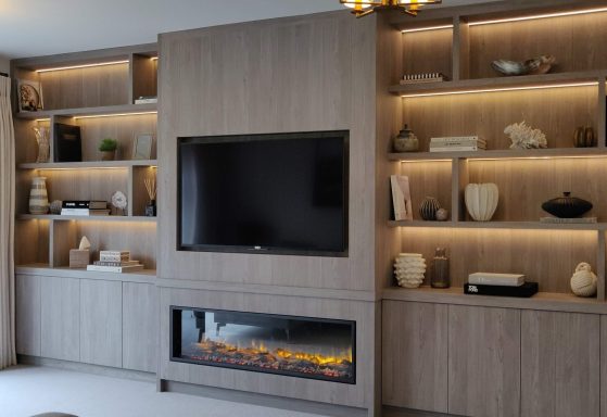 Nordic Grey display shelving with central TV panel and LED fire Modern living room with a wall unit, TV, and an electric fireplace under soft lighting.