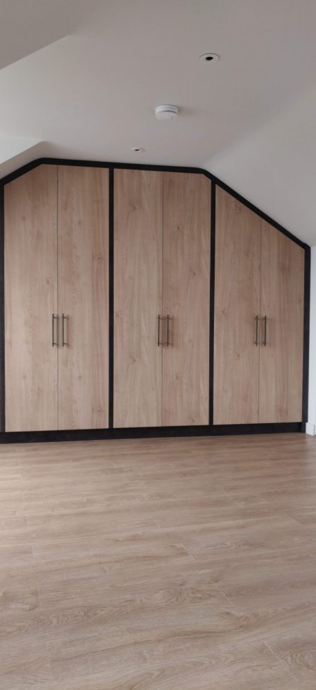Natural Kendal Oak fitted wardrobes Modern room with sloped ceiling, featuring wooden cabinetry along one wall.