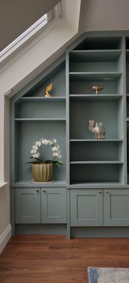 Fijord Green display shelving with central TV panel Light blue shelving unit with decorative items and a potted plant against a slanted wall.