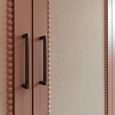 Antique rose finish wardrobes featuring elegant arched panel detailing, integrated top ventilation grilles, bobble bead details. Close-up of a decorative cabinet door with textured finish and black handles.