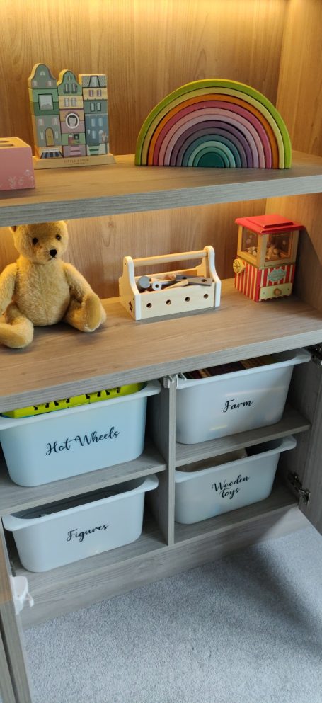 Grey Nordic Wood open shelving with LED's. Surrounding storage A modern room with a wooden shelf displaying various toys and decorative items.