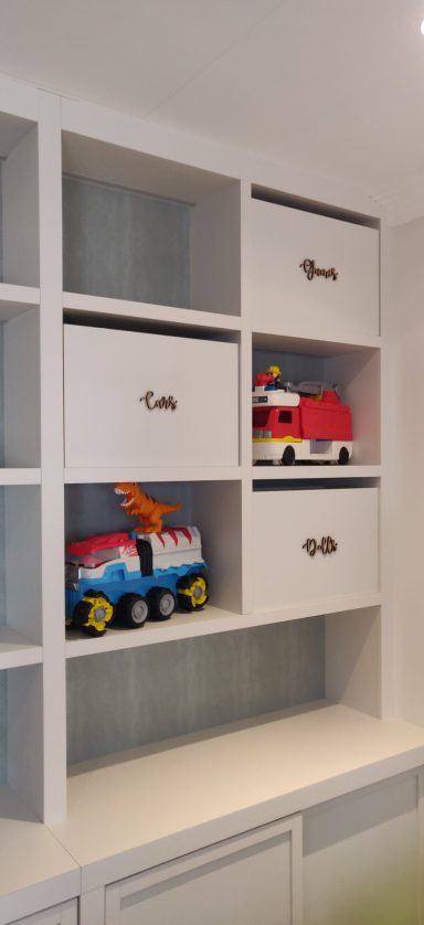 Colourful toy fire truck and construction vehicle on white shelving unit.