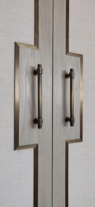 Stained oak door detail with antique brass trimming detail Stylish double door handles on a sleek, beige panel with decorative framing.